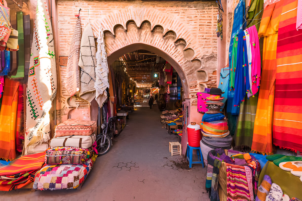 Sunlit archway leading into a textile-lined alley of the Marrakech Medina