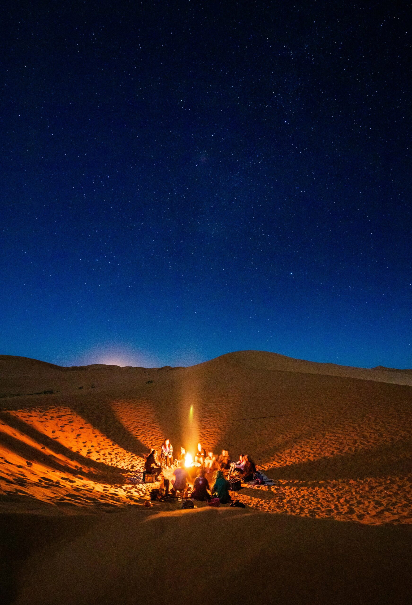 Travellers gathered around a fire at a desert camp beneath a star-filled sky